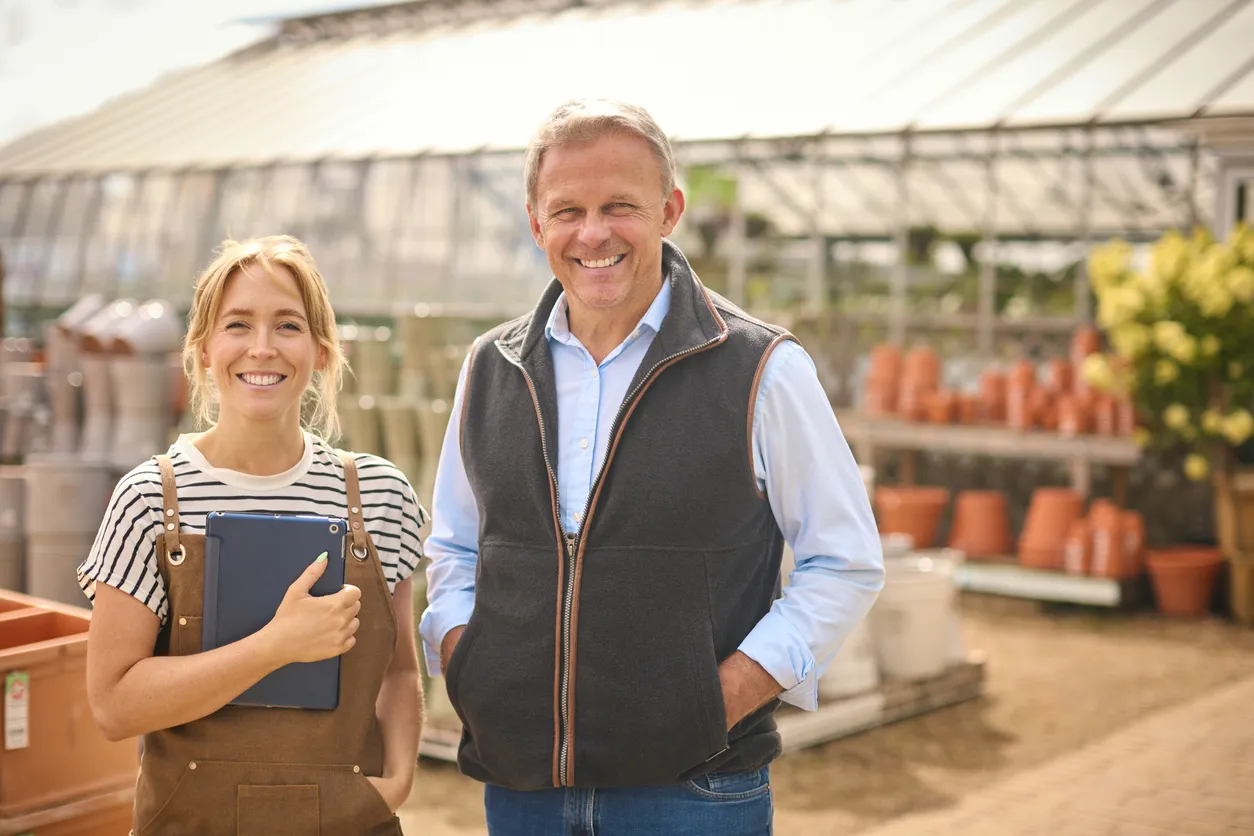 Business Owners Thriving With Trusted Guidance From Matt Uhler Two small business owners smiling confidently outside their greenhouse, representing success through trusted business advisory support